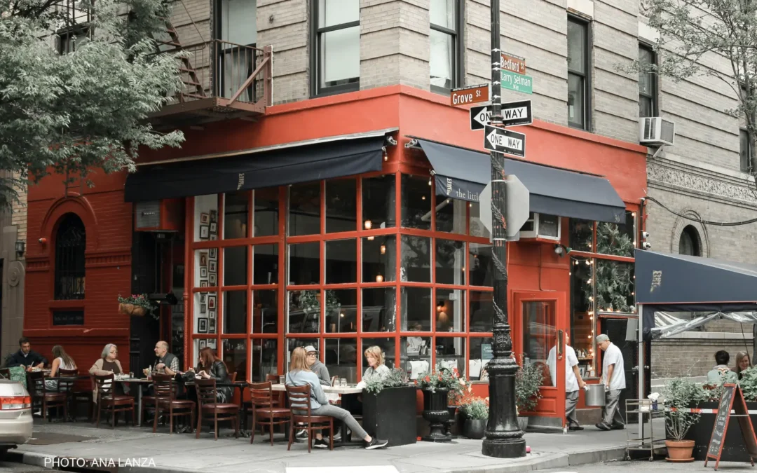 Outdoor dining scene at a red corner café on a busy city street with people seated outside.